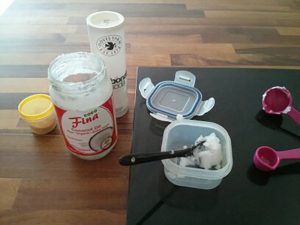 Coconut oil jar and other ingredients with measuring spoons and a plastic container.