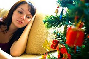 Female lying down on a sofa looking ill or sad next to a Christmas tree