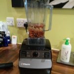 A blender on a kitchen surface with almonds and water in it.