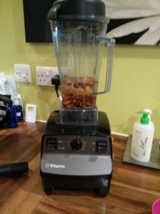 A blender on a kitchen surface with almonds and water in it.