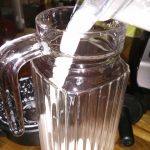 Pouring freshly made almond milk into a glass storage jug