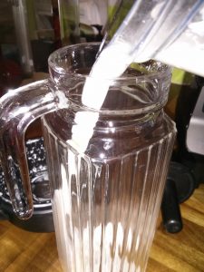 Pouring freshly made almond milk into a glass storage jug