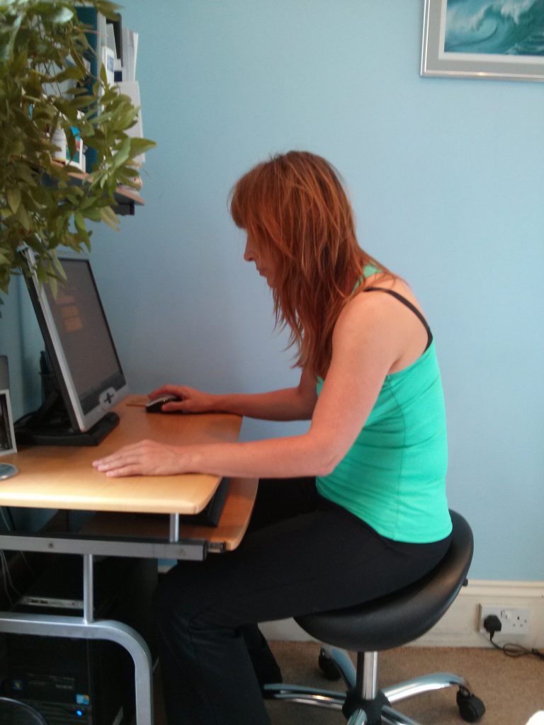 demostrating poor sitting posture with anterior head carriage, rolled forward shoulder position 